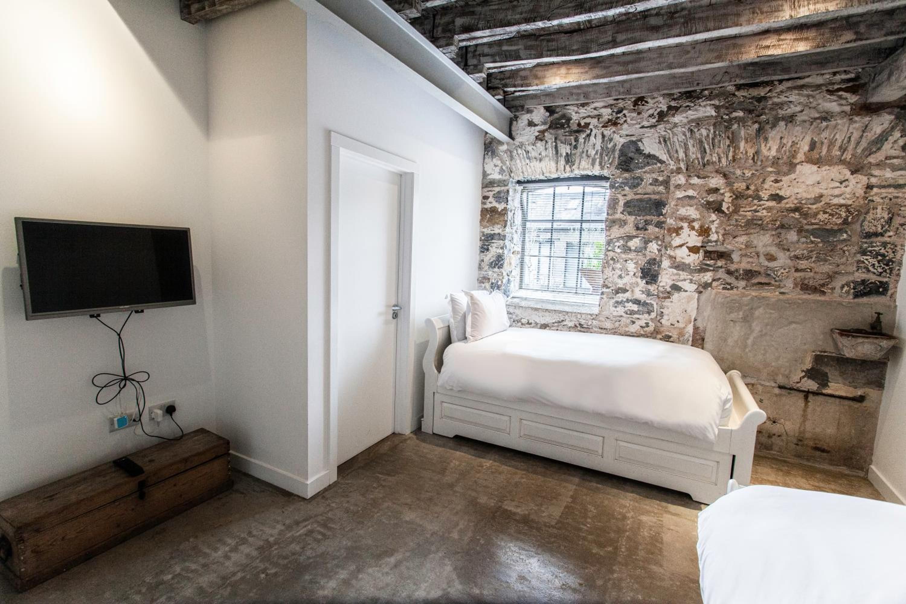 A bedroom with a stone wall, a bed, a television mounted on the wall, and a window.