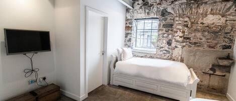 A bedroom with a stone wall, a bed, a television mounted on the wall, and a window.