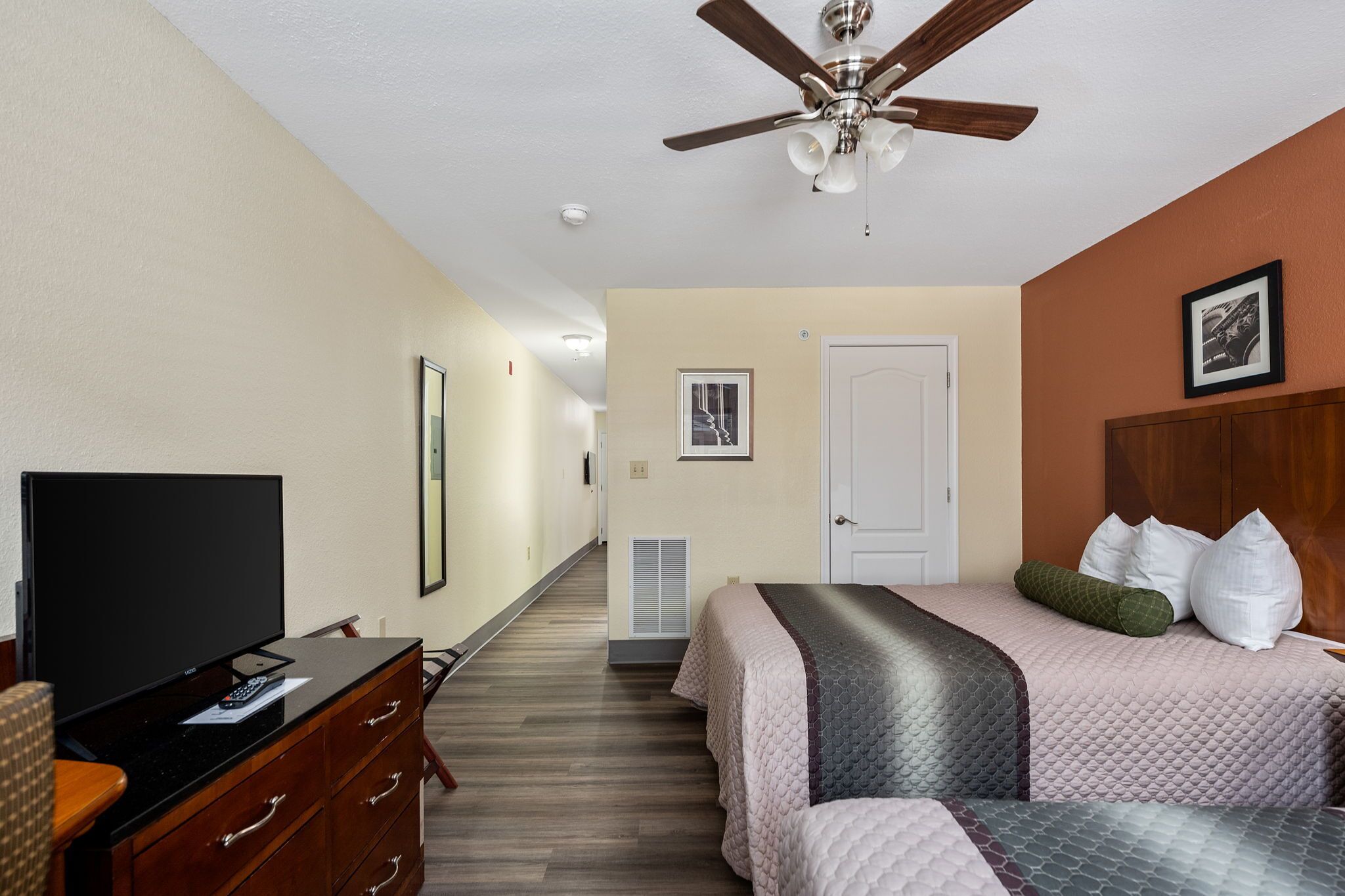 A hotel room with a bed, a TV, a ceiling fan, and a door.