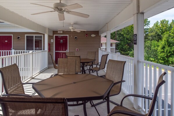 A covered outdoor seating area with a table and chairs, a ceiling fan, and a view of the surrounding greenery. - Affordable Suites of America Quantico (Stafford)