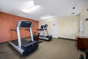 A fitness room with treadmills and an elliptical machine, carpeted floor, and a wooden cabinet. - Affordable Suites of America Quantico (Stafford)