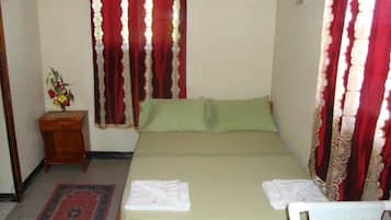 Un dormitorio con cama, almohadas, una mesita de noche, un jarrón con flores y cortinas.