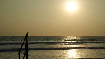 A beach with a wooden structure, waves, and the sun setting or rising.