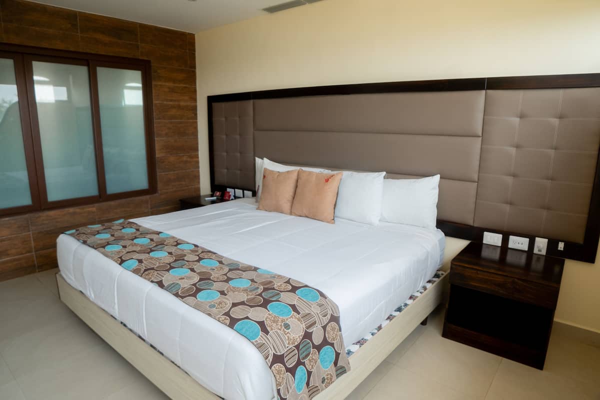 Una cama grande con colcha estampada, cabecera de madera y mesita de noche con lámpara.