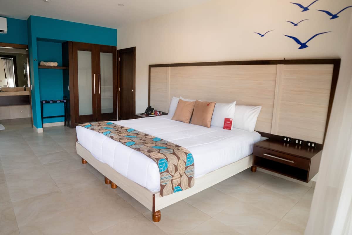 Habitación de hotel con una cama grande, una mesita de noche, un armario y un baño visible a través de una puerta abierta.
