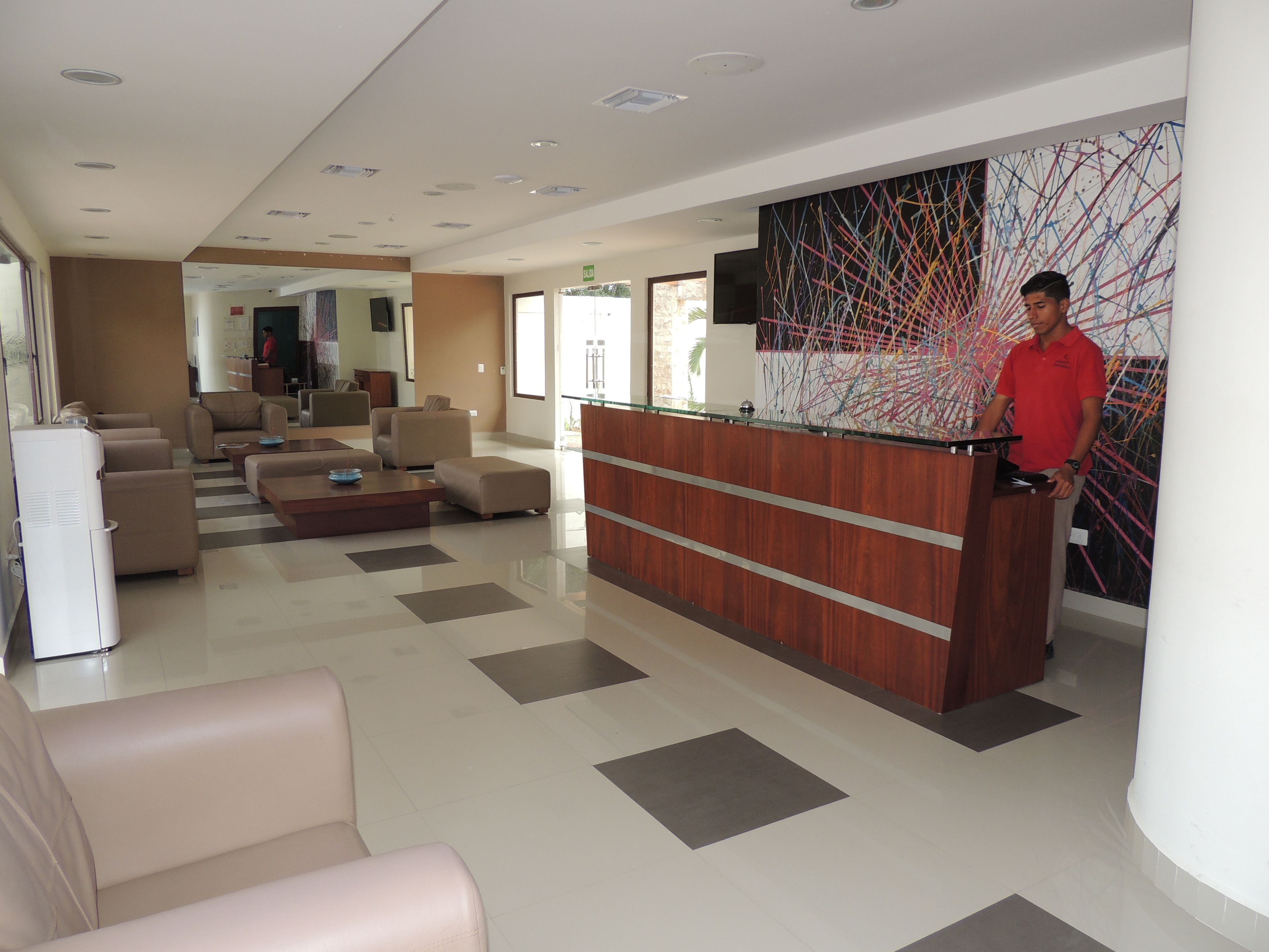 Un vestíbulo moderno de hotel con mostrador de recepción, zona de estar y una gran obra de arte abstracta en la pared.