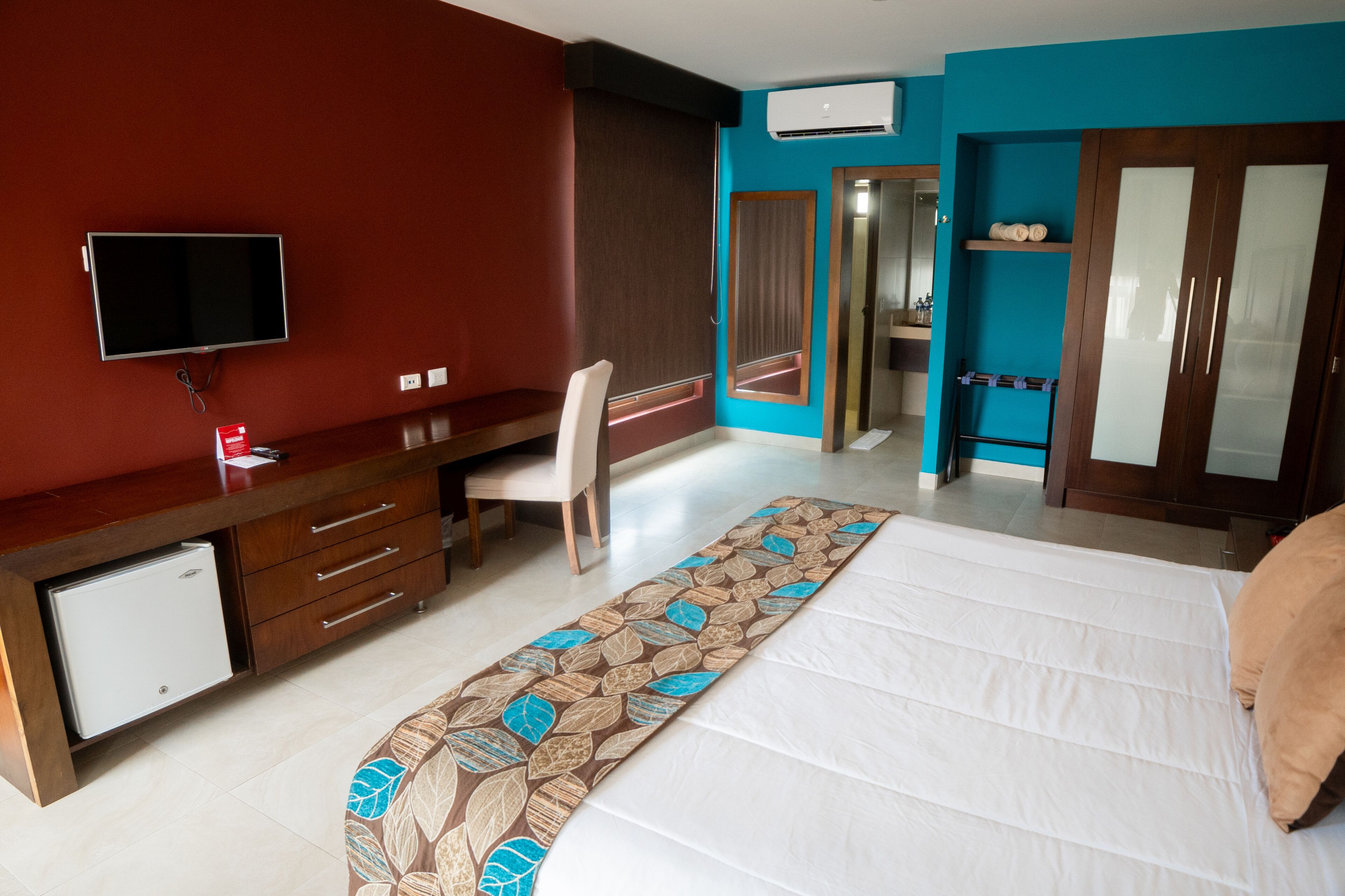 Una habitación de hotel con cama, escritorio, silla, televisor, armario y baño.