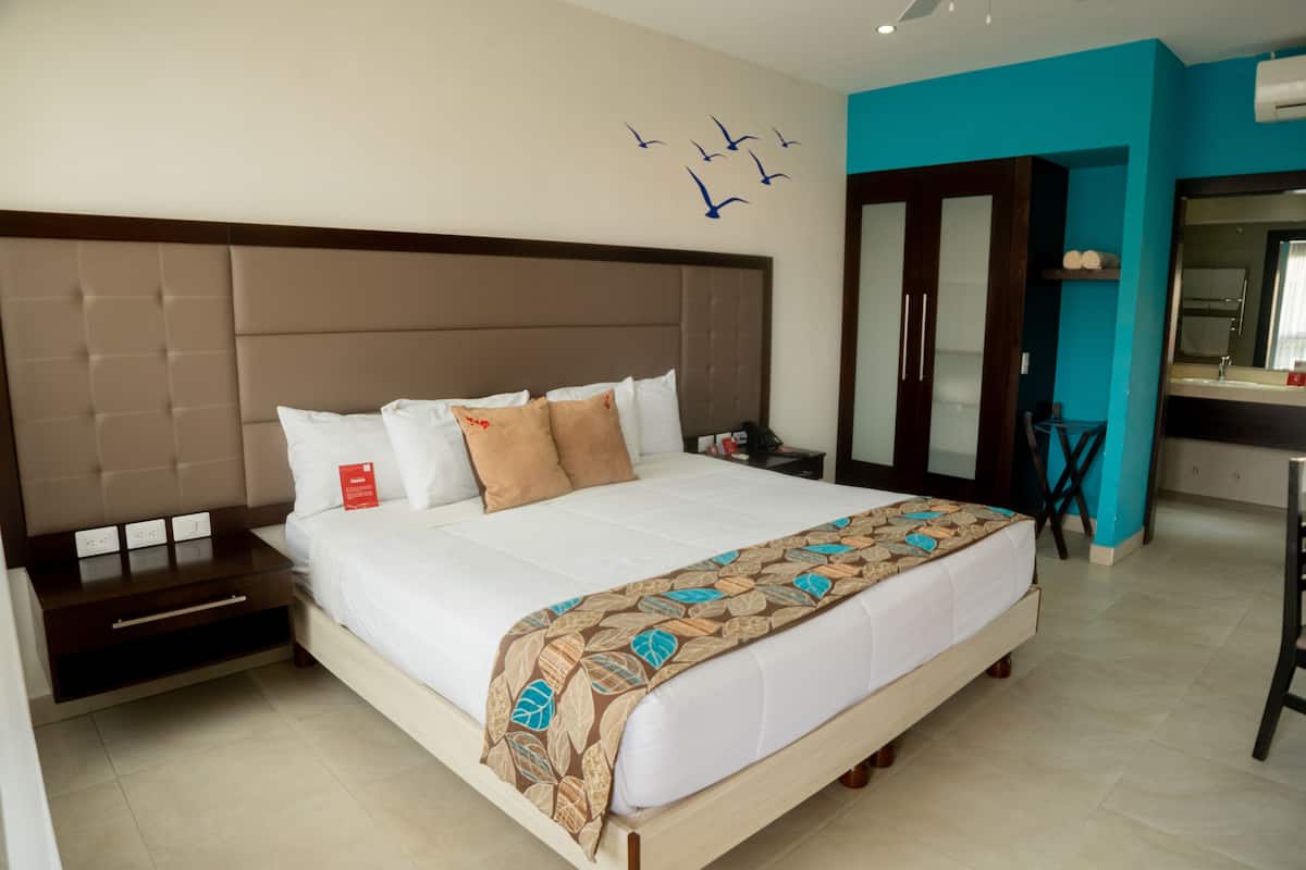 Habitación de hotel con una cama grande, una mesita de noche, un escritorio y un baño con espejo.