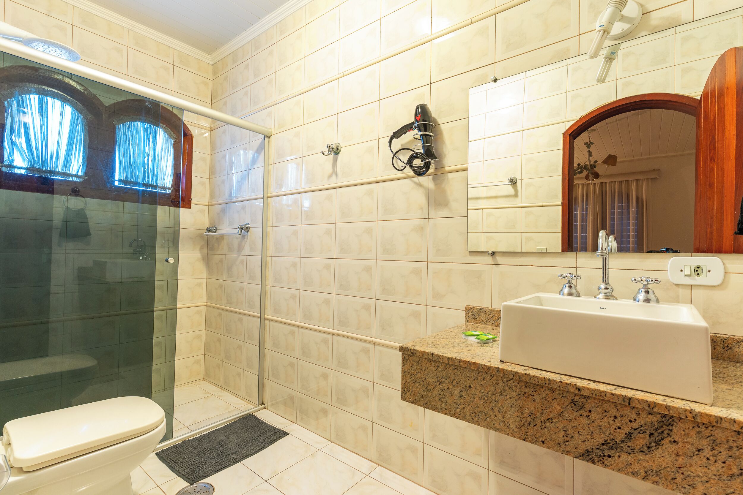 A bathroom with a glass-enclosed shower, a white sink, and a mirror with an arched frame.