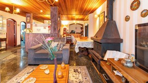 A cozy living room with a fireplace, wooden ceiling, and a dining area in the background. - Pousada Recanto Sião (Campos do Jordão)