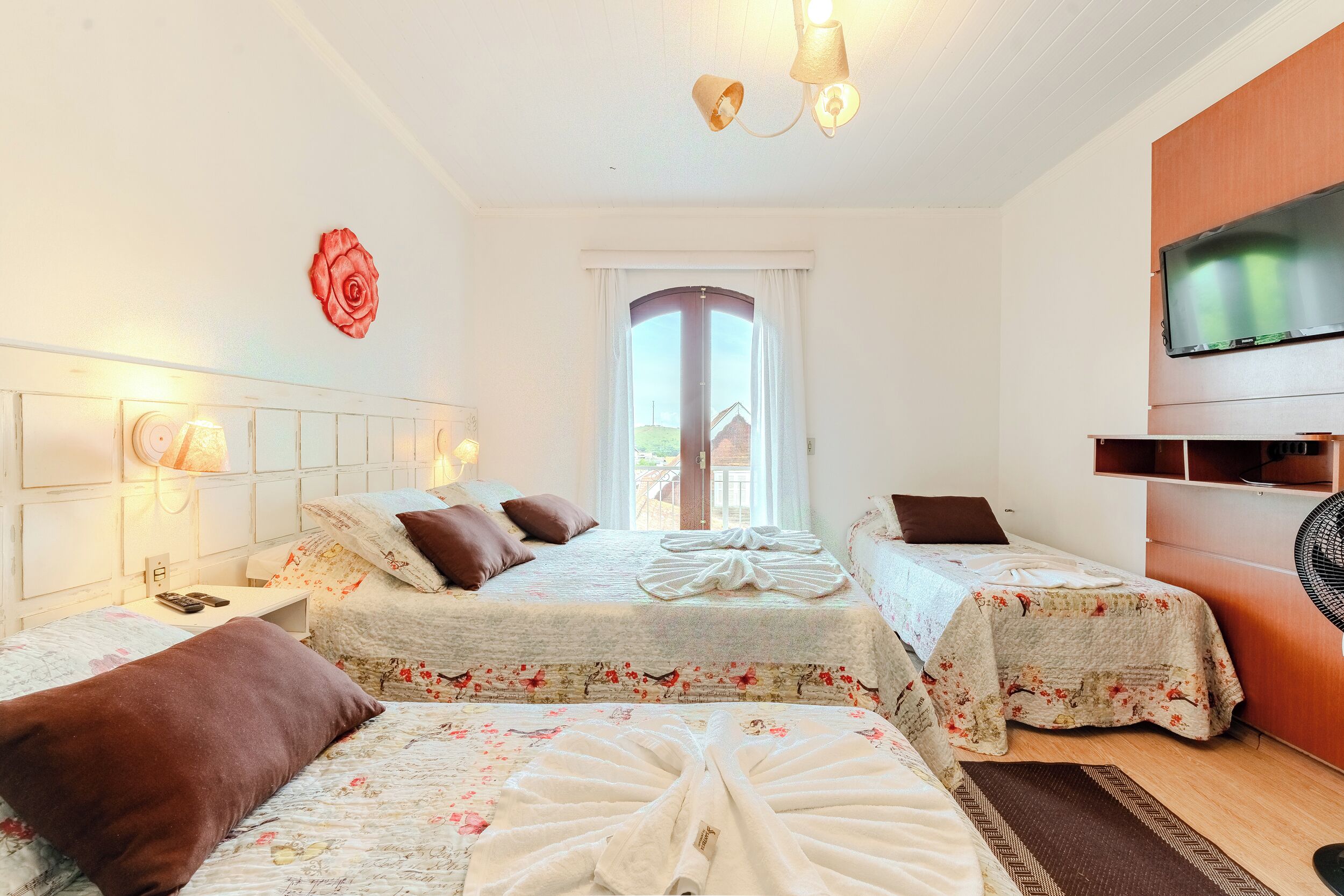 A hotel room with two beds, a TV, a window with curtains, and a decorative rose on the wall.