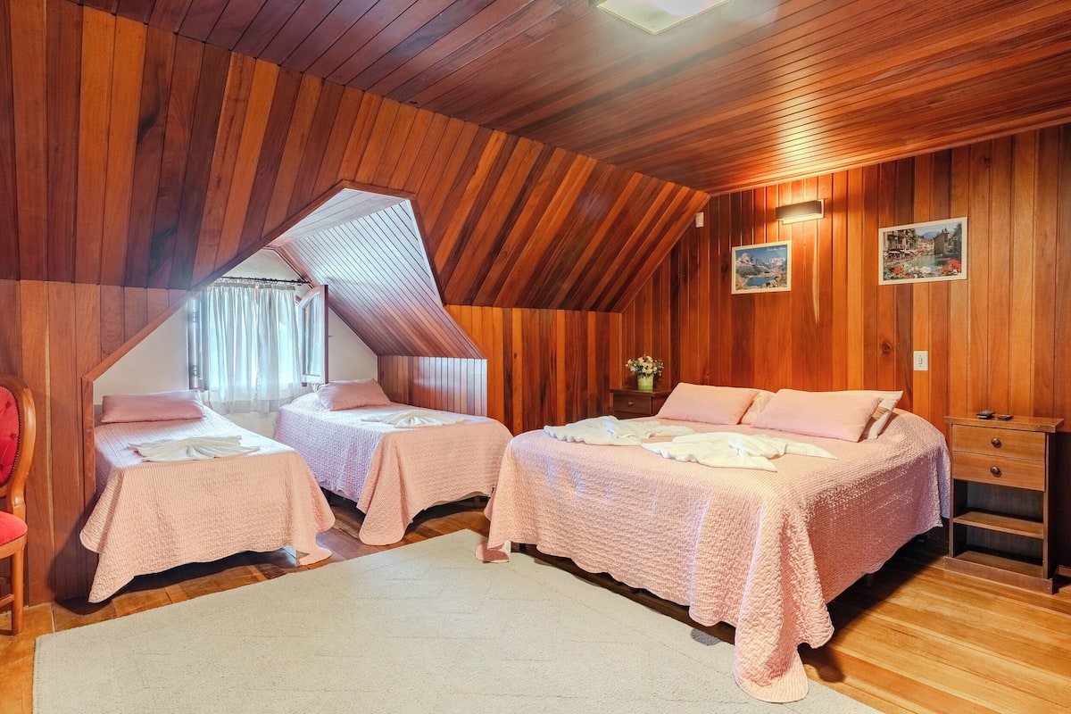 Quarto com duas camas, paredes de madeira, teto inclinado e uma mesinha de cabeceira.
