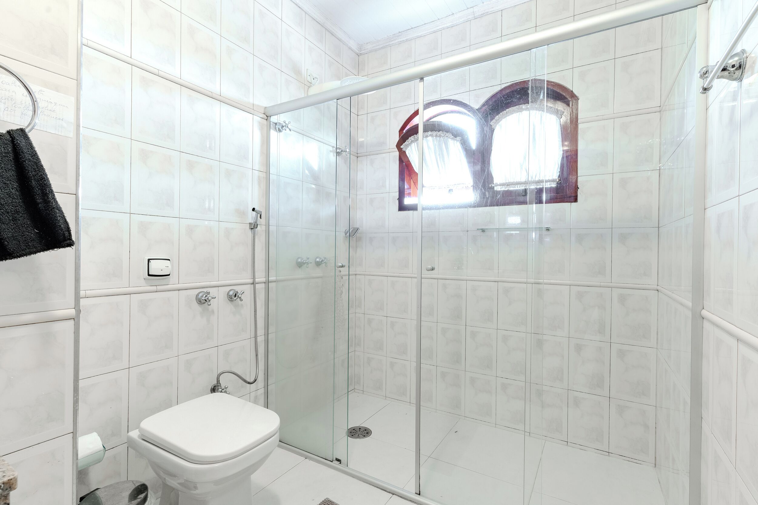 Une salle de bain moderne avec une douche à parois de verre, des toilettes et une fenêtre surmontée d’une arche décorative.