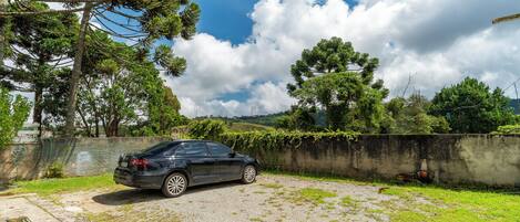A black car parked on a gravel driveway with a grassy area and a concrete wall in the background.