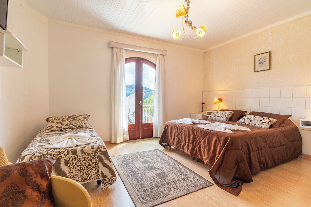 Quarto com duas camas, uma janela grande com cortinas, um candelabro e vista para o exterior.