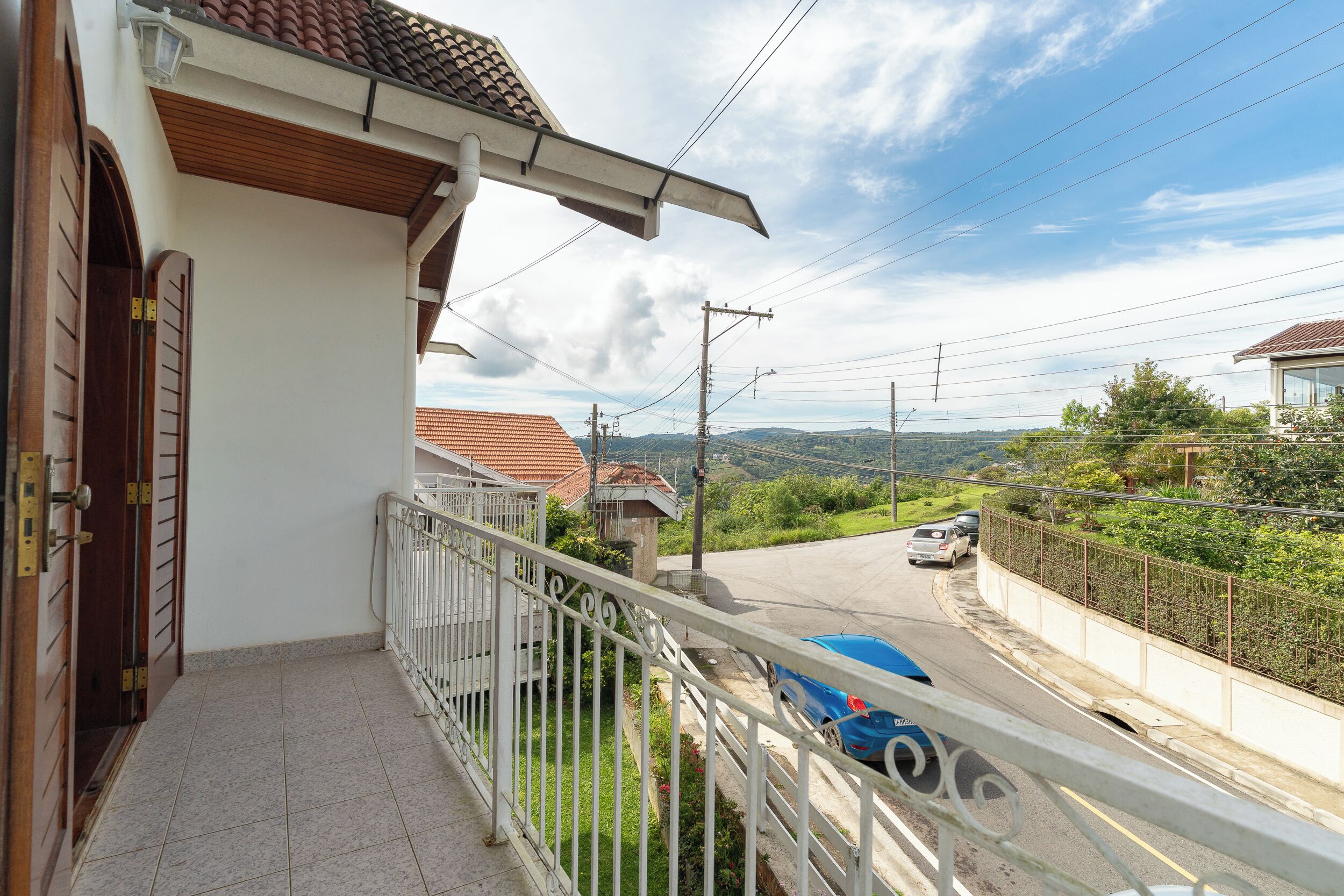 A balcony with a white railing overlooking a road with cars and greenery.