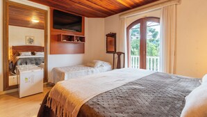 A cozy room with a wooden ceiling, a bed with a textured blanket, a small table with glasses, and a TV mounted on the wall. - Pousada Recanto Sião (Campos do Jordão)