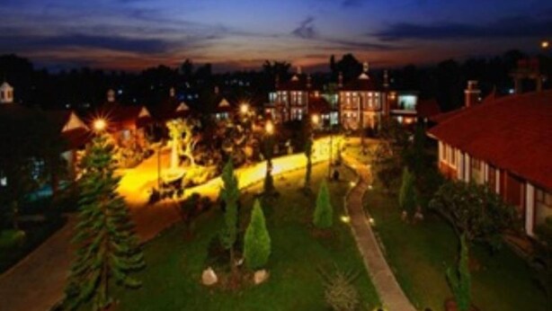 Un edificio grande y luminoso con múltiples ventanales y un jardín con senderos y árboles.