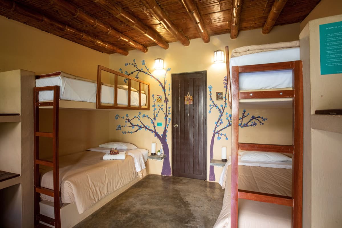 A dormitory room with bunk beds, a wooden ceiling, and a door with a tree mural.