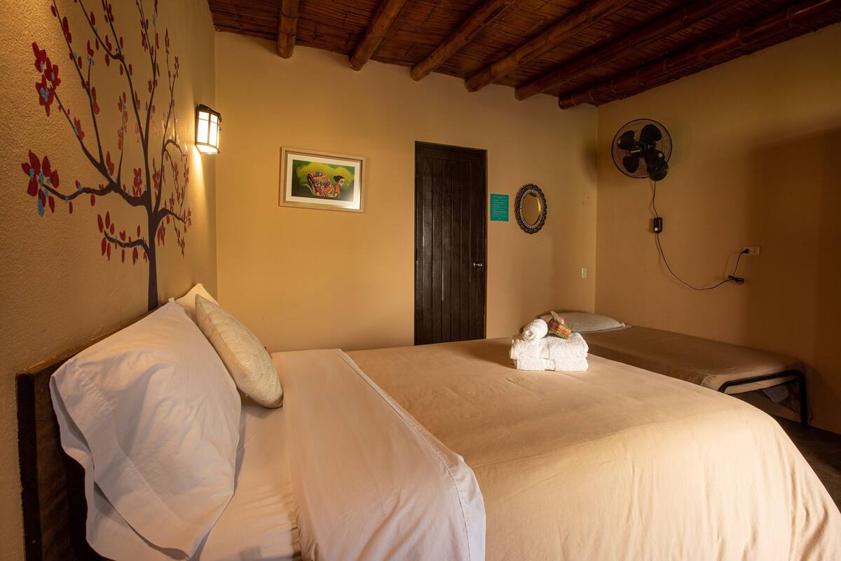 A hotel room with a large bed, a bedside table, a wall-mounted fan, and a door with a mirror.
