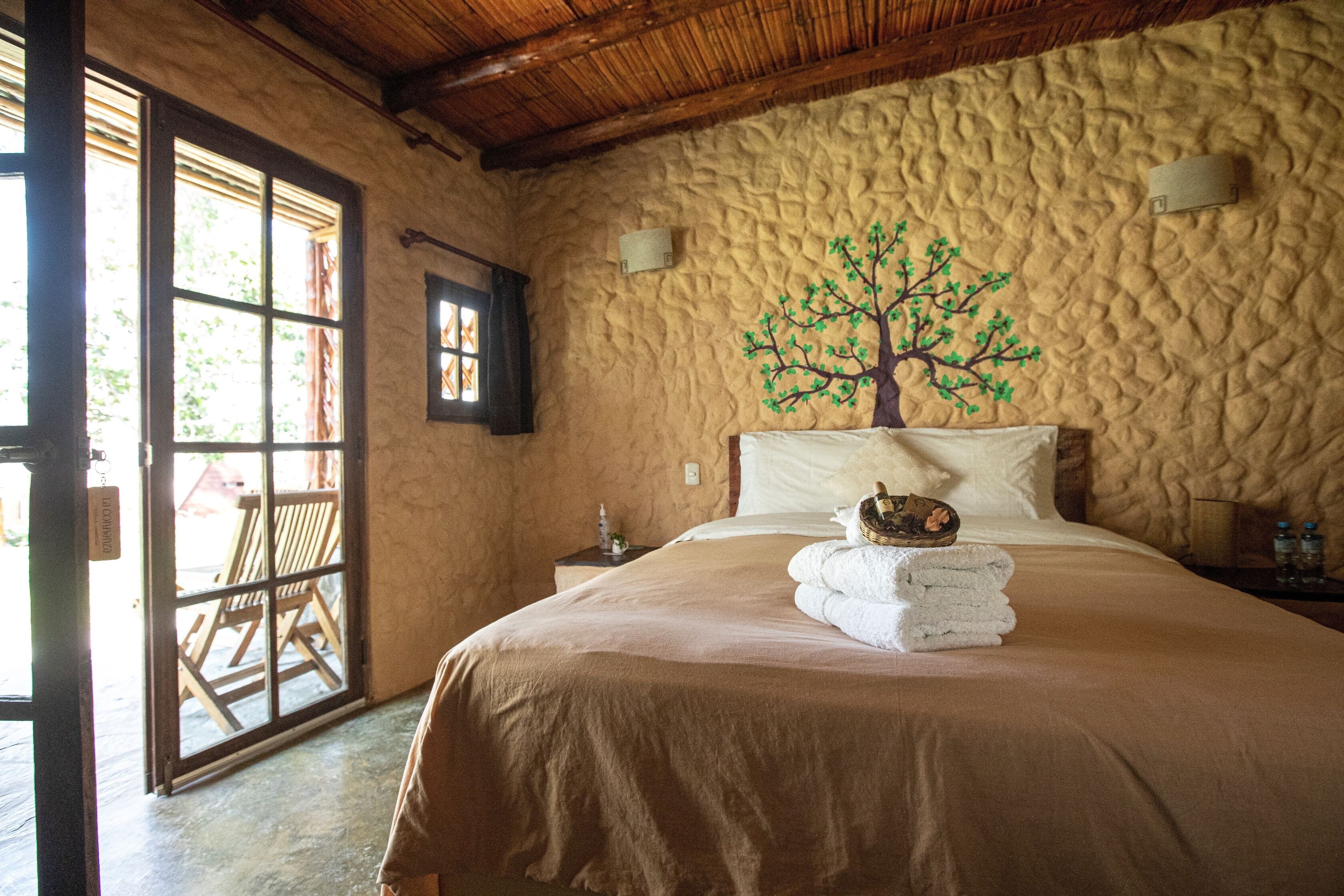 Un dormitorio con una cama grande, techo de madera, pared texturizada y ventana con vistas al exterior.