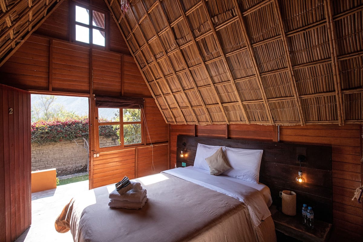 A wooden room with a bed, a window, and a door leading outside.