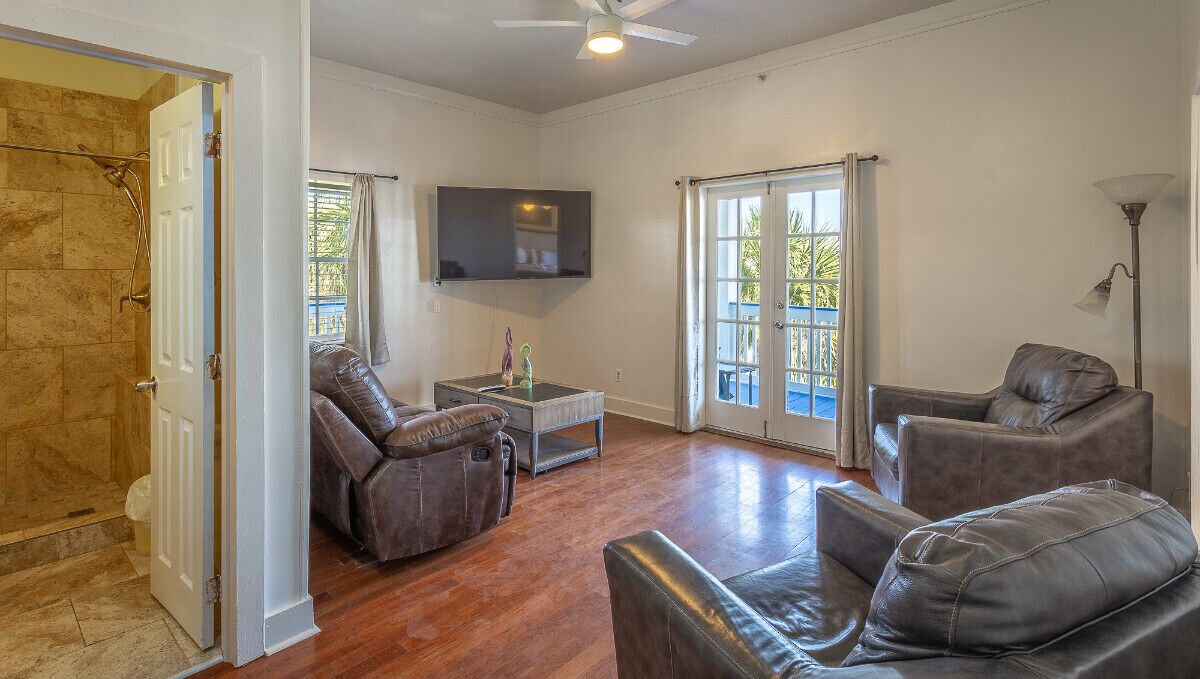 A spacious living room with leather sofas, a flat-screen TV, and a ceiling fan.