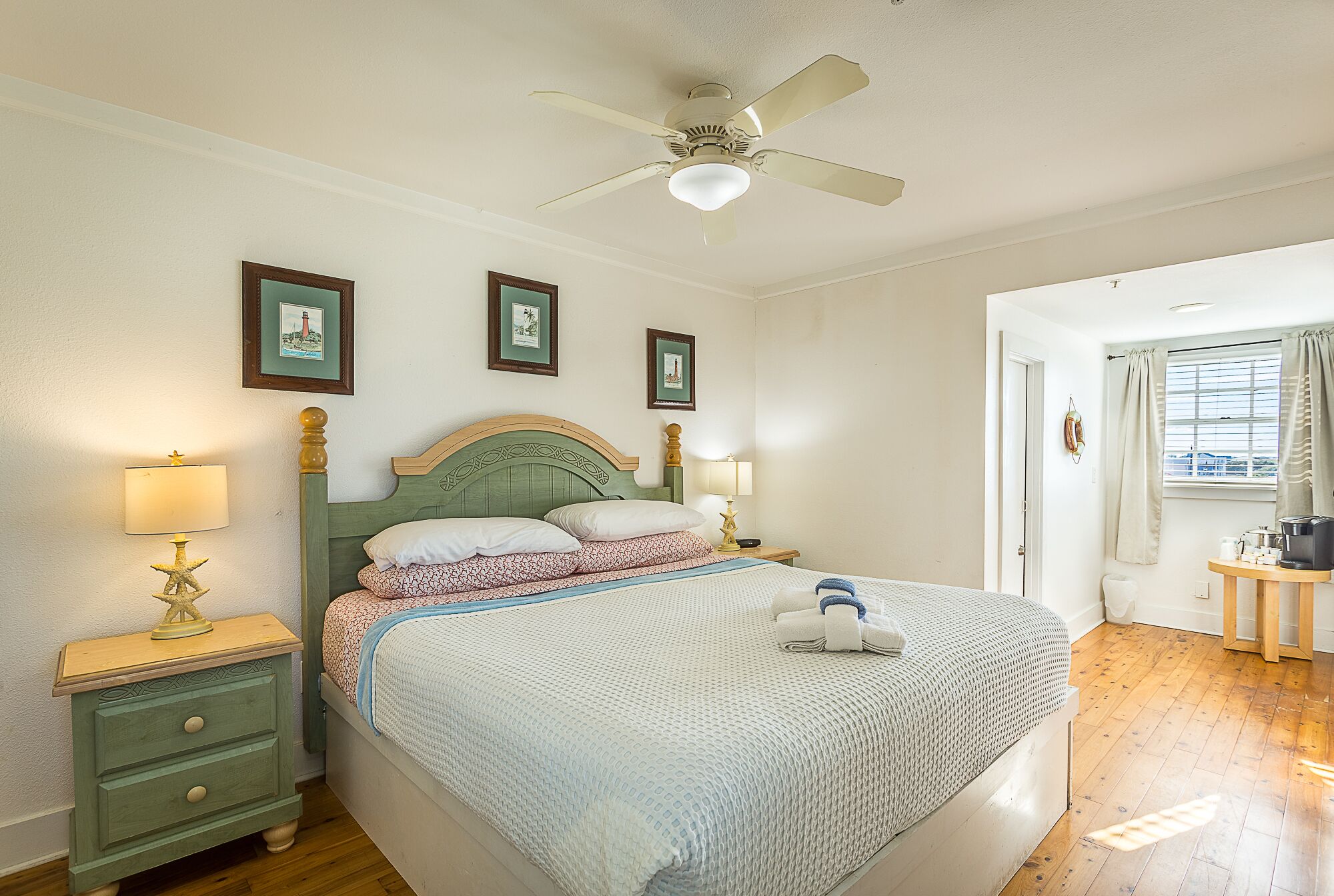 A neatly arranged bedroom with a bed, bedside tables, a ceiling fan, and framed pictures on the wall.