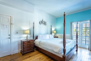 A four-poster bed with a wooden frame, a dresser with drawers, a wall-mounted ship decoration, and a door with a notice.