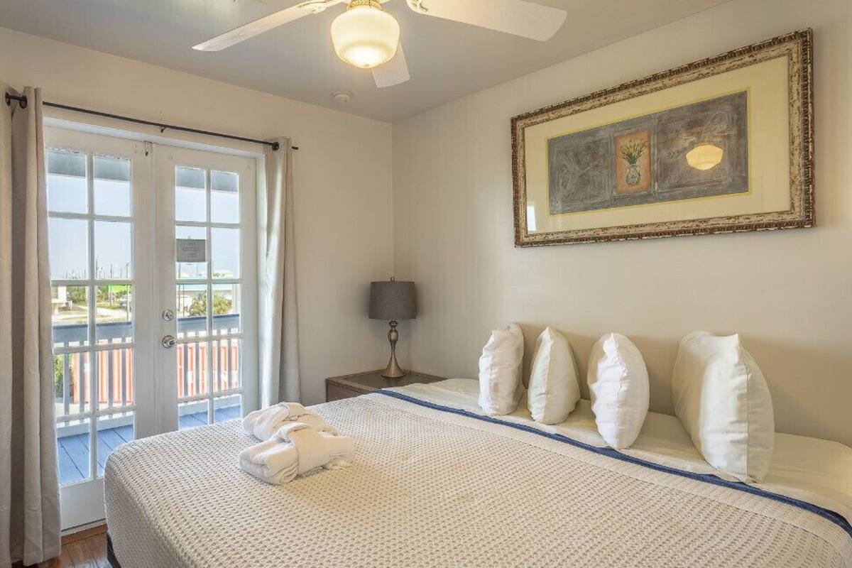 Une chambre d’hôtel avec un lit, une table de chevet, une lampe, un tableau encadré au mur et un balcon avec vue.