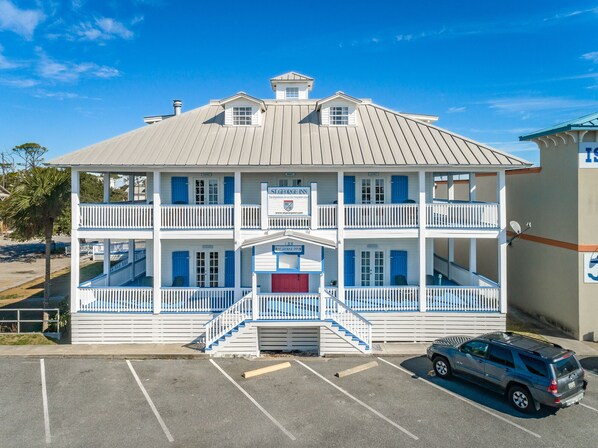 A two-story building with a balcony on each floor, a central staircase, and a parking lot in front.