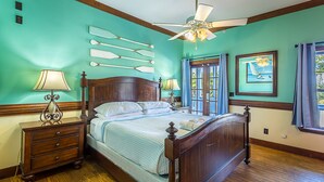 A bedroom with a wooden bed, two bedside tables with lamps, a ceiling fan, and a window with curtains. - St. George Inn (St. George Island)