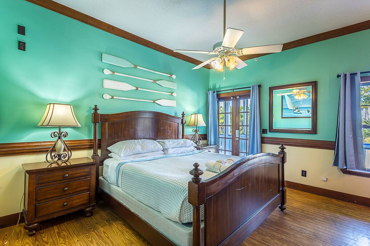 Une chambre à coucher avec un lit en bois, deux tables de chevet avec des lampes, un ventilateur de plafond et une fenêtre avec des rideaux.