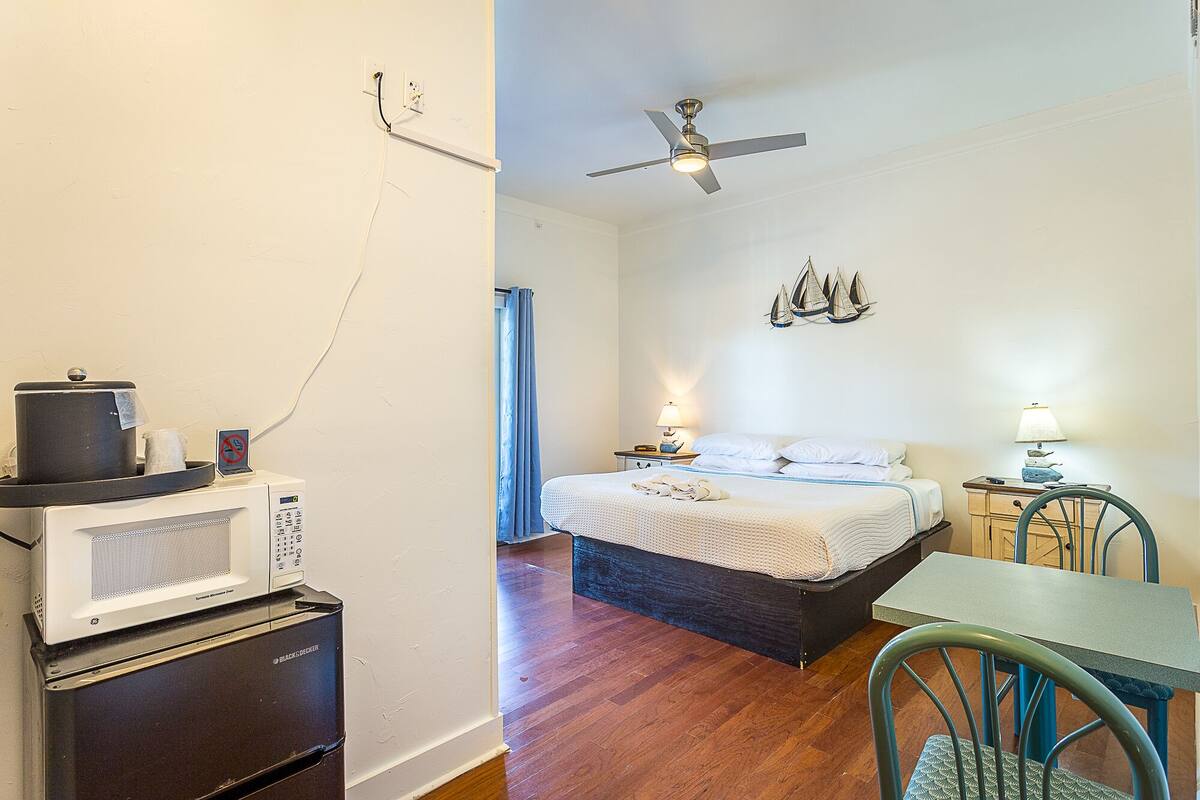 Une chambre d’hôtel équipée d’un lit, d’un bureau, d’une chaise, d’un ventilateur de plafond et d’un four à micro-ondes.