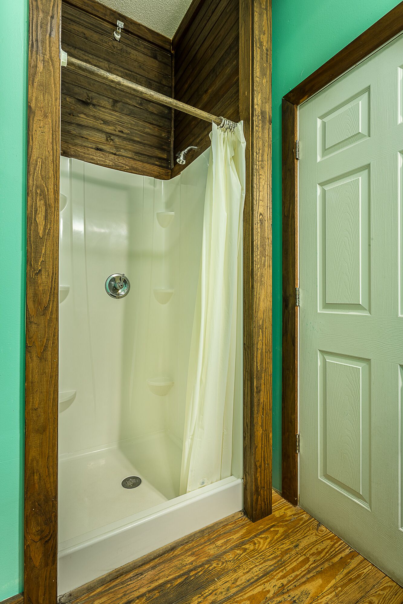 Un bagno con cabina doccia in legno, una vasca da bagno bianca e una porta verde.