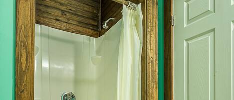 Een badkamer met een douchecabine van hout, een witte badkuip en een groene deur.