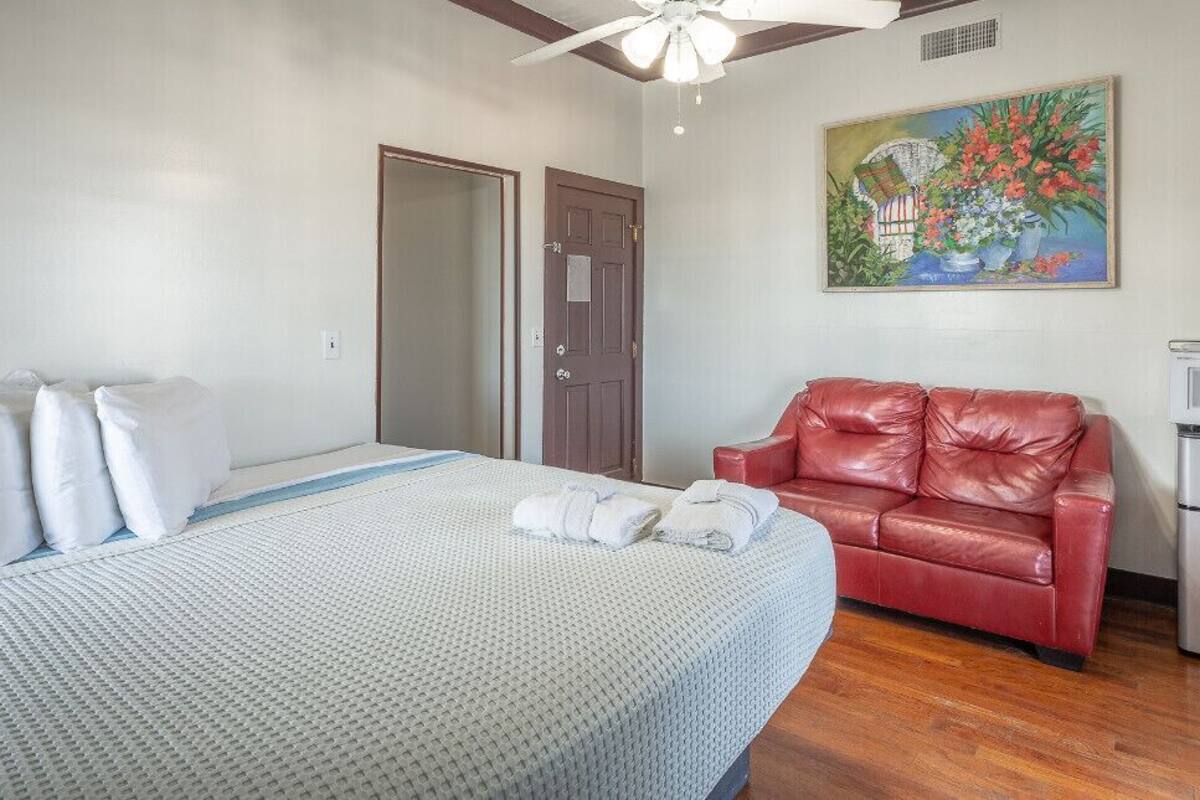 Une chambre d’hôtel avec un lit, un canapé en cuir rouge, un tableau au mur et une kitchenette.