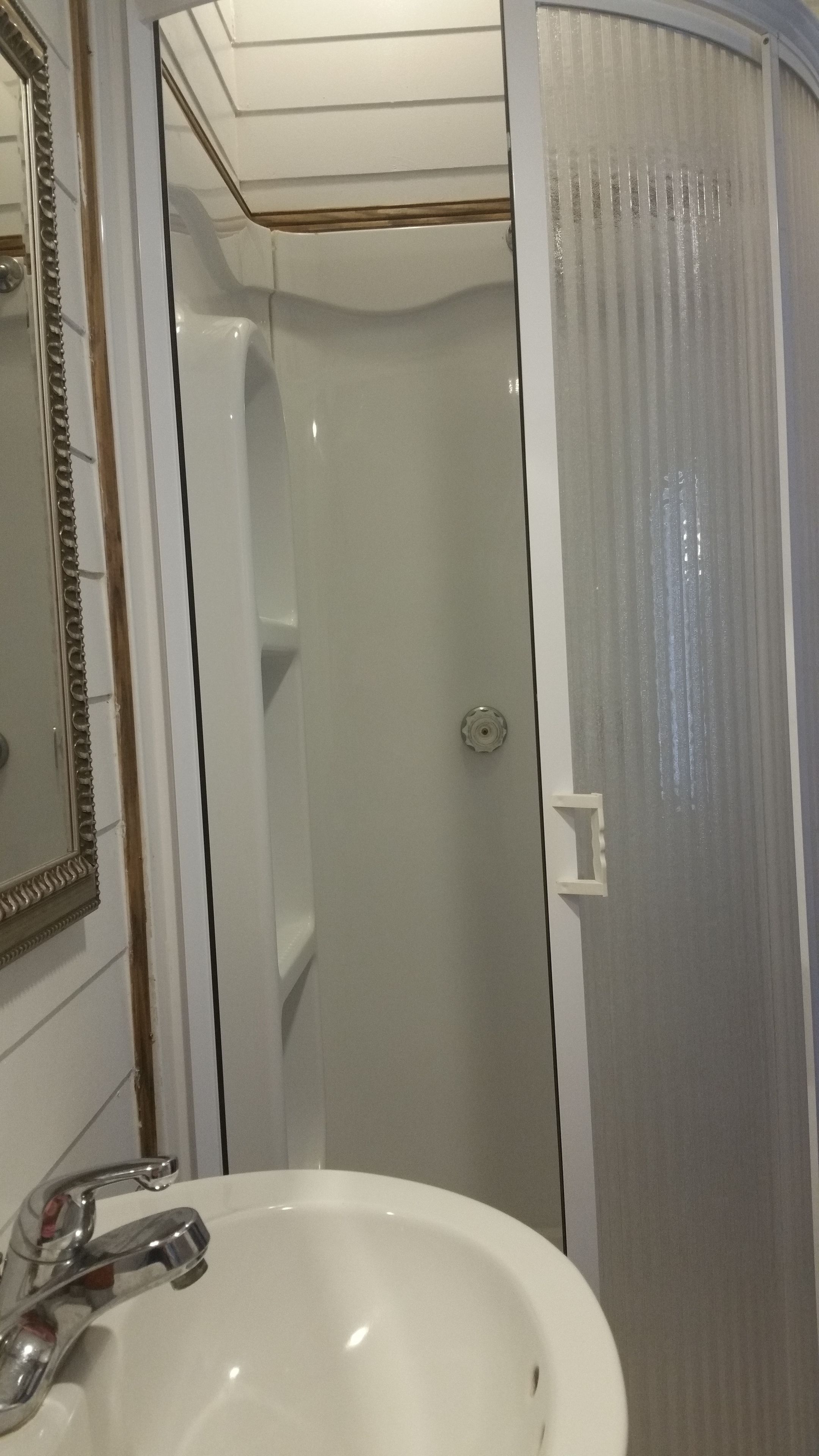Un baño con lavamanos blanco, espejo con marco decorativo y ducha con puerta de cristal.