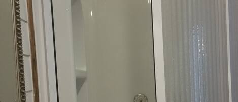 Un baño con lavamanos blanco, espejo con marco decorativo y ducha con puerta de cristal.