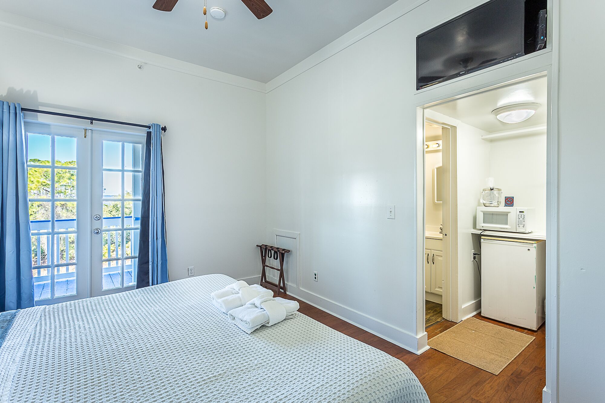 Un dormitorio con cama, escritorio, microondas y baño visible a través de una puerta abierta.