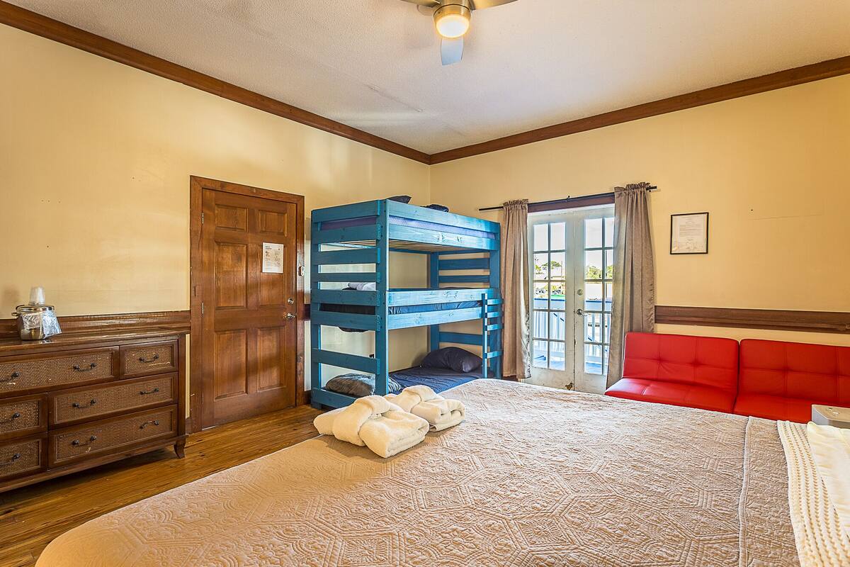 Une chambre avec un lit superposé, une commode en bois, un canapé rouge et un grand lit recouvert d’une couvre-lit à motifs.