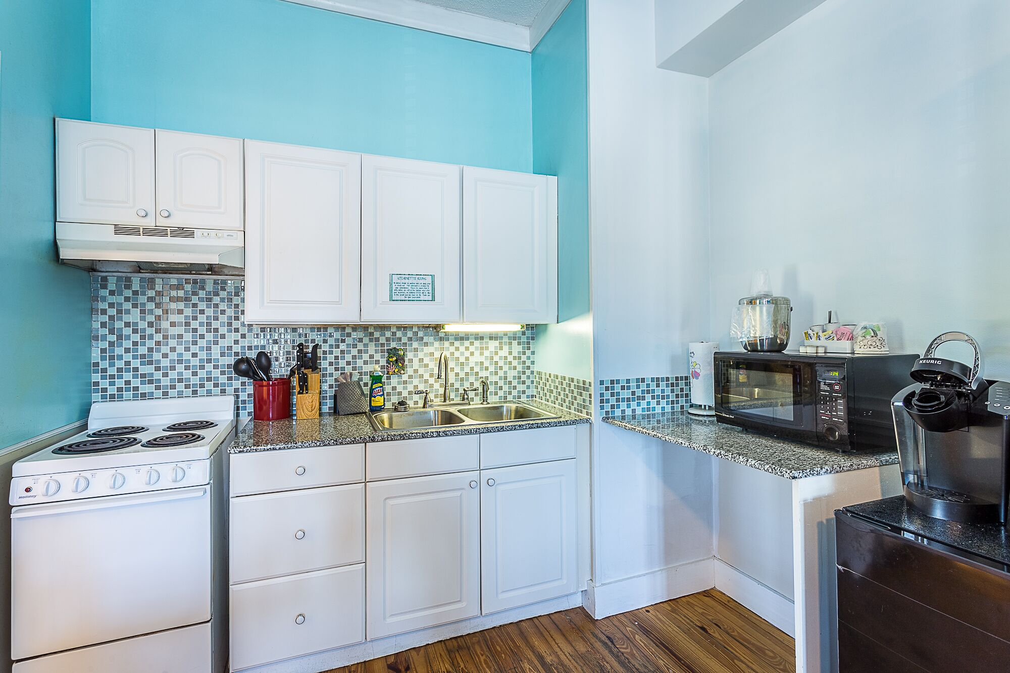 A kitchen with white cabinets, a stove, a microwave, and a sink.