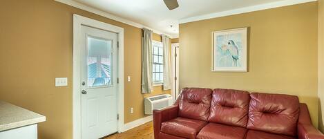 A living room with a red leather couch, a ceiling fan, a door with blinds, and a radiator.