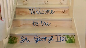 A staircase with a nautical-themed design, including a lighthouse and waves, leading to a landing with a sign that reads "Welcome to the St. George Inn." - St. George Inn (St. George Island)