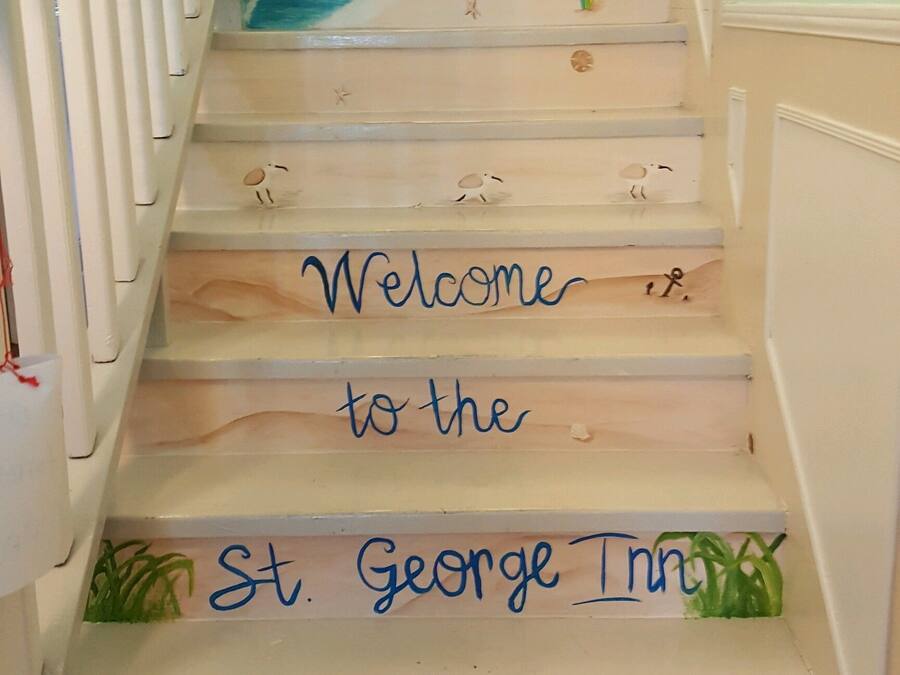 A staircase with a nautical-themed design, including a lighthouse and waves, leading to a landing with a sign that reads "Welcome to the St. George Inn."