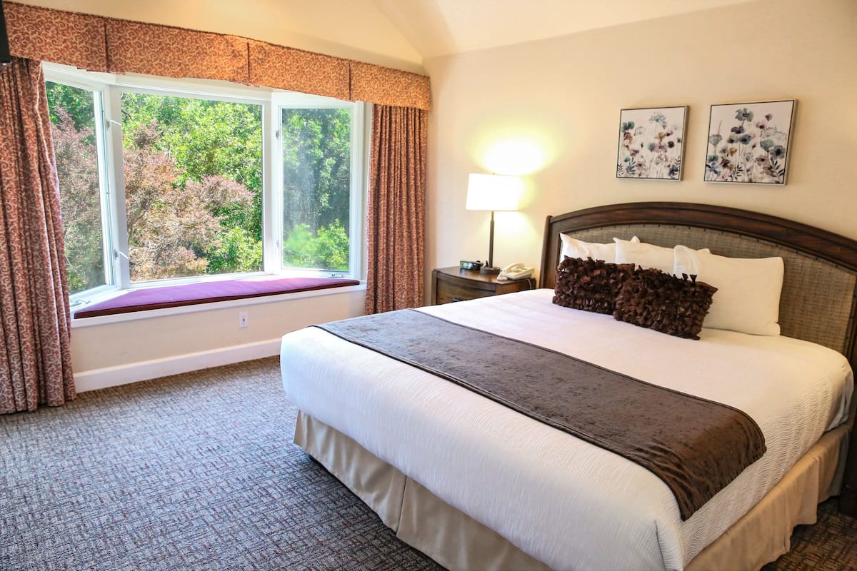 A hotel room with a large bed, a window with curtains, a bedside lamp, and two floral wall art pieces.
