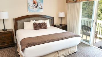 A hotel room with a large bed, two bedside tables with lamps, a painting of a bird on the wall, and a view of the outdoors through a sliding door.