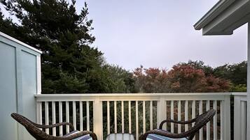 A balcony with two wicker chairs and a small table, surrounded by a white railing.