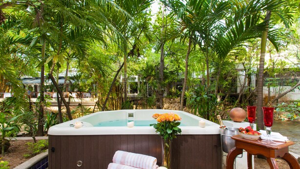 A hot tub surrounded by lush greenery, with towels and a vase of flowers on a wooden table nearby. - Garlands del Rio Riverside Boutique Hotel (Puerto Vallarta)