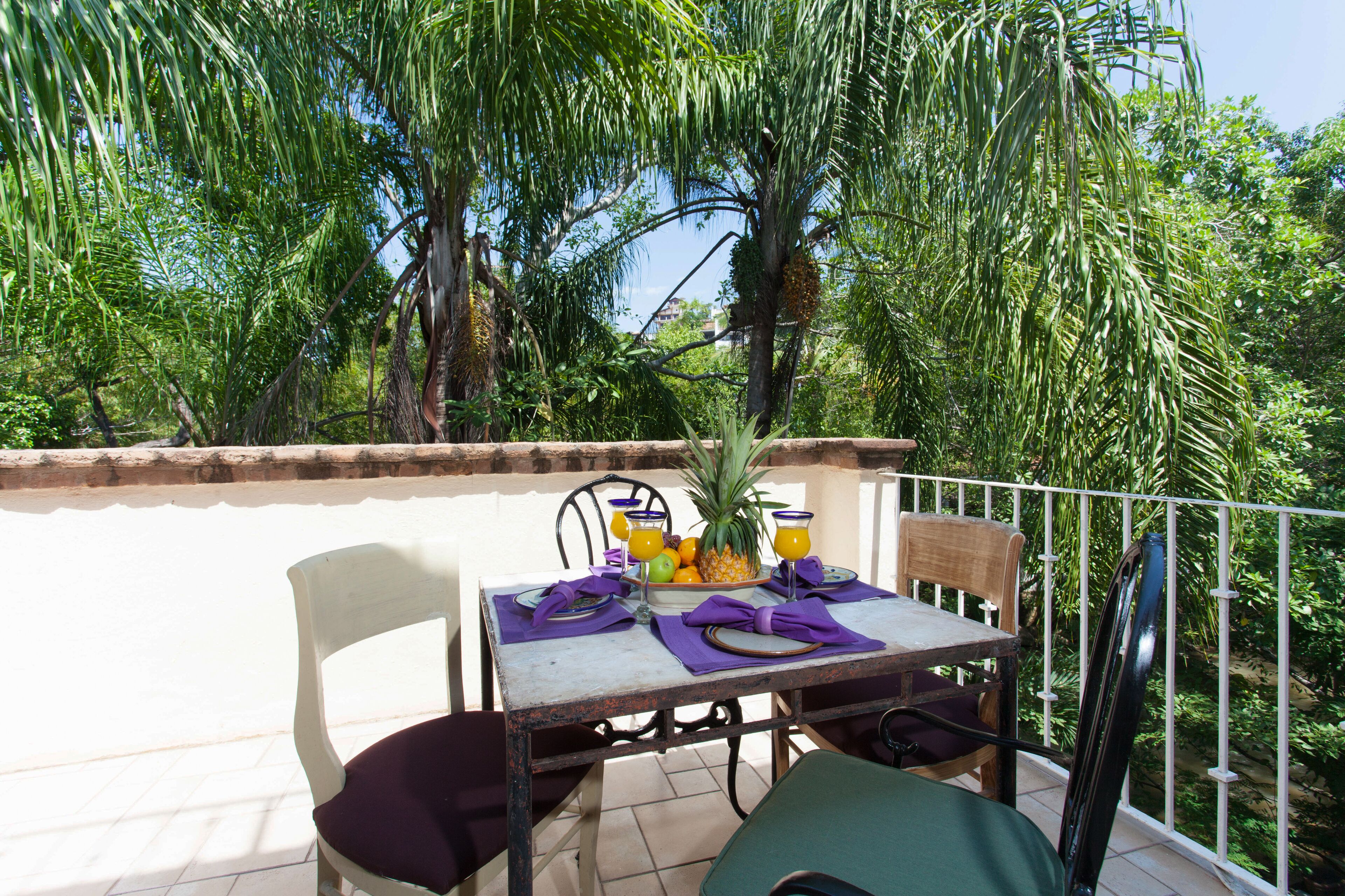 A balcony with a table set for two, surrounded by lush greenery.
